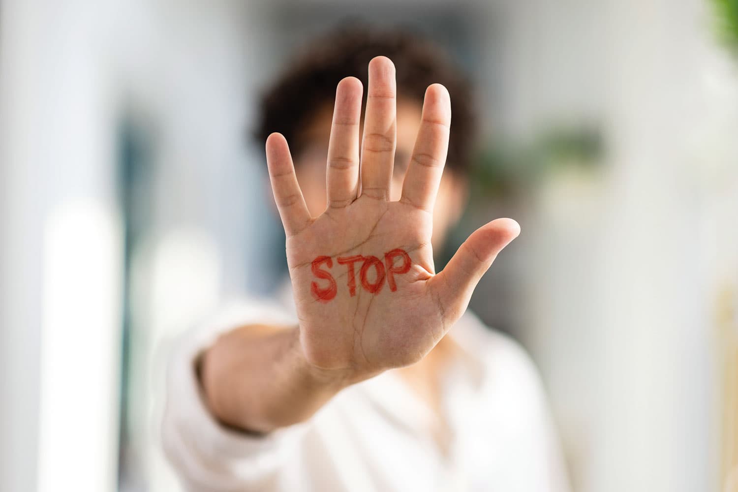 close-up of someone’s hand held up in front of them with the word ‘STOP’ written in red ink on their palm