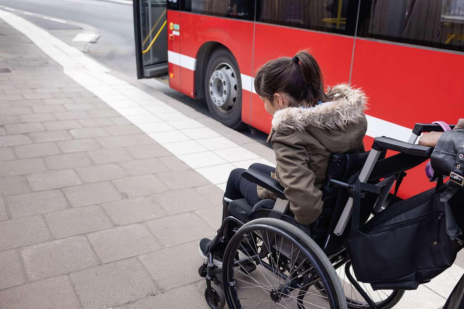 photo from behind of older girl in wheelchair alongside a bus