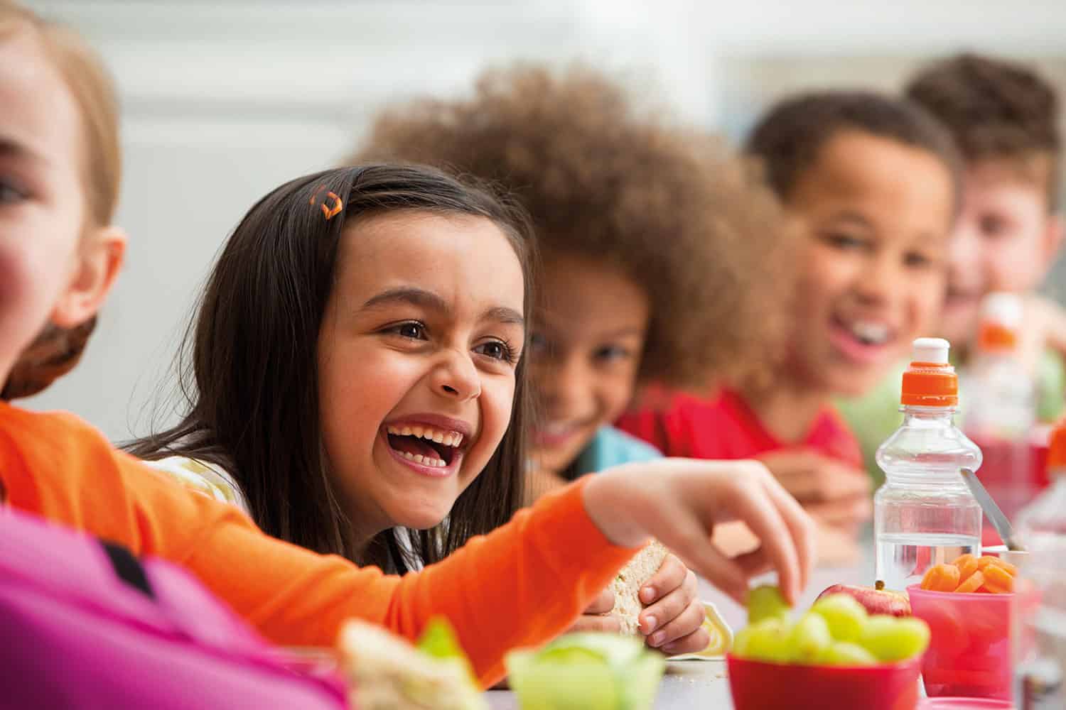 diverse group of children eating healthy snacks, close up on a laughing girl