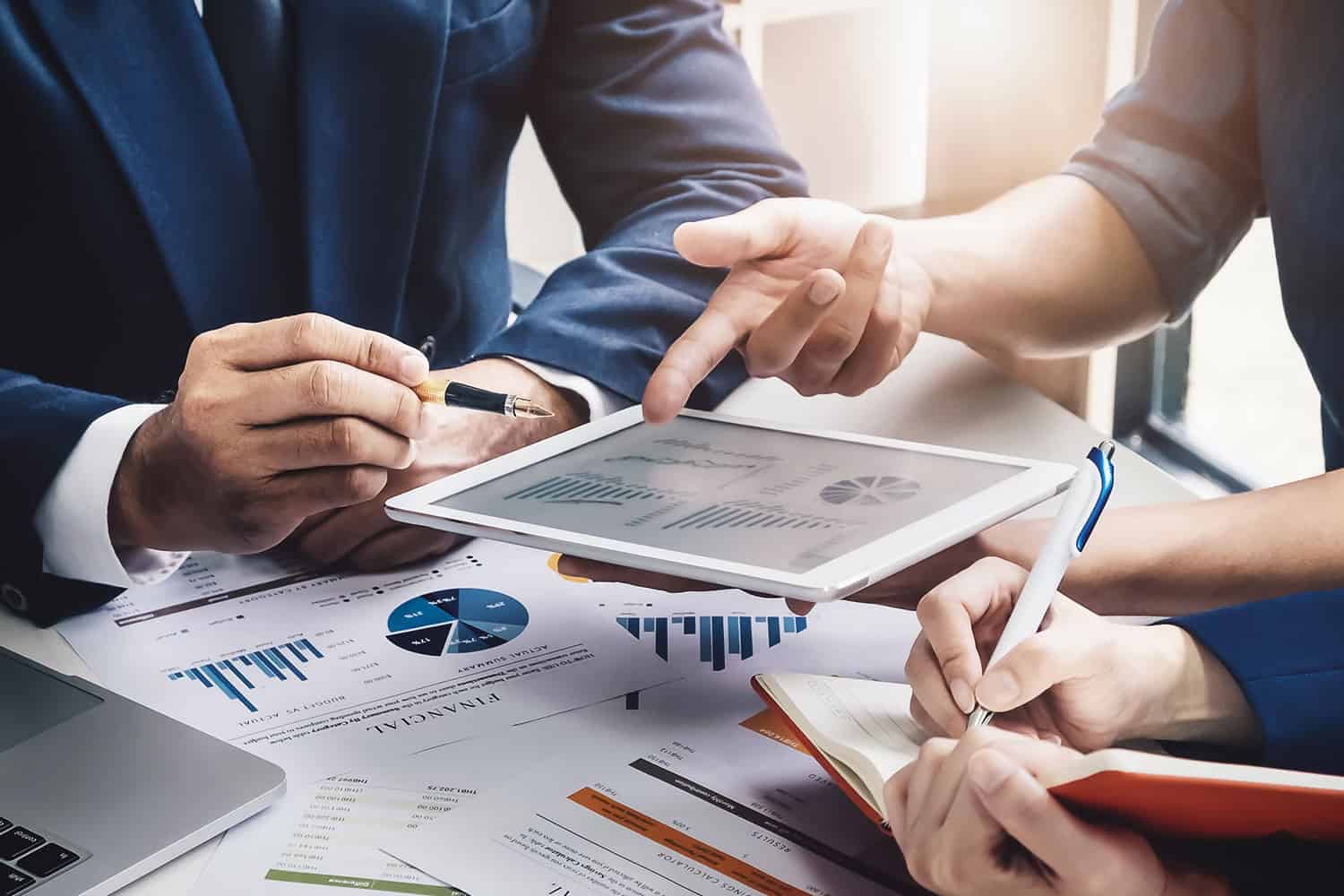 close-up on hands holding and pointing at financial reports on graphs on paper and a tablet on desk
